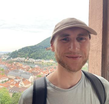 man in light shirt and baseball hat looks at camera